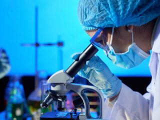 Profile view of concentrated Asian microbiologist examining sample with help of modern microscope while wrapped up in work at dim laboratory